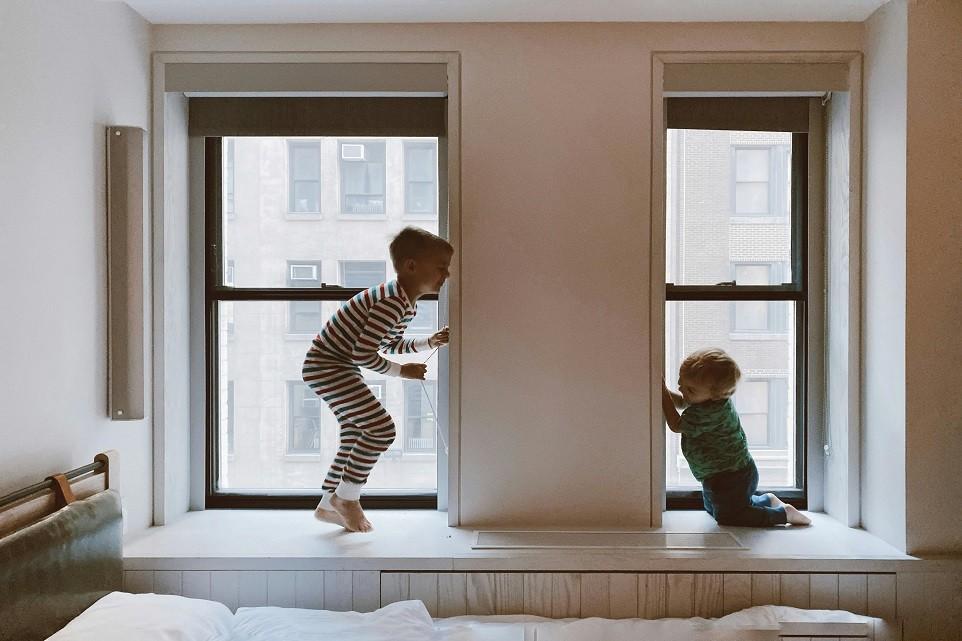 Two young children playing near windows inside home during school holidays in Singapore